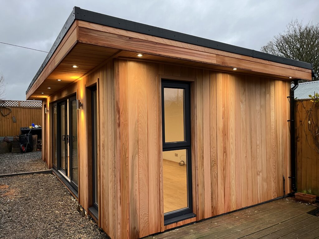Showcasing the bespoke canopy overhang of this Crusoe Garden Room including canopy and downlights to the front and both sides of the garden room helping form a beautiful courtyard garden. This garden room was handcrafted as a music studio to house a grand piano.