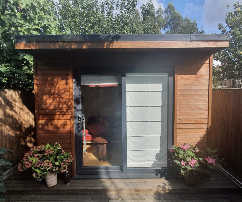 A very cute cedar clad Crusoe Compact with pots of flowers either side of the black sliding patio doors.
